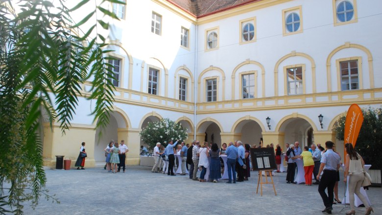 Tafeln im Weinviertel, © Weinviertel Tourismus GmbH Menschen versammeln sich in einem historischen Schlosshof mit gelb-weißen Fassaden.