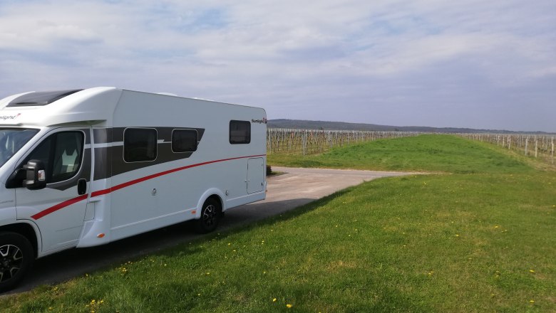 Motorhome parking space, © Weingut Studeny Motorhome on a pitch next to a vineyard under a blue sky.