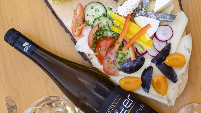Heurigenplatte, © Weinviertel Tourismus GmbH / Schwarz-König Heurigenplatte mit Aufschnitt, Käse, Gemüse und Wein auf einem Holztisch.