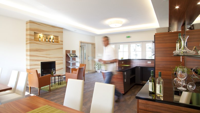 Verkostungsraum, © Astrid Bartl Ein moderner Verkostungsraum mit Holzmöbeln, Weinflaschen und einem unscharfen Mann im Vordergrund.