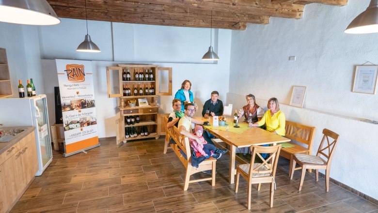 Eine Gruppe von Menschen sitzt an einem Tisch in einem gemütlichen Raum mit Holzboden und -decke.