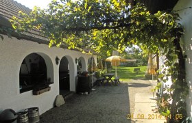 Ein gemütlicher Gasthof mit weißen Bögen, grüner Laube und gelben Sonnenschirmen im Garten.