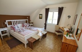 Gemütliches Gästezimmer mit Doppelbett, Sofa, Tisch und Stuhl. Braune Akzentwand und dunkle Vorhänge.