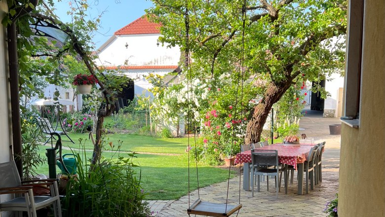 Herzlich Willkommen, © Gästehaus Weinwurm Ein idyllischer Garten mit einer Schaukel, einem Tisch mit Stühlen und blühenden Pflanzen.