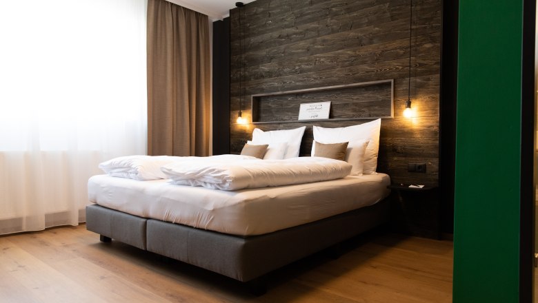 Modernes Hotelzimmer mit großem Bett, Holzwand und hängenden Lampen.