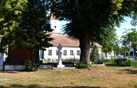 Ein Platz mit großen Bäumen, einer Statue und einem Gebäude im Hintergrund.