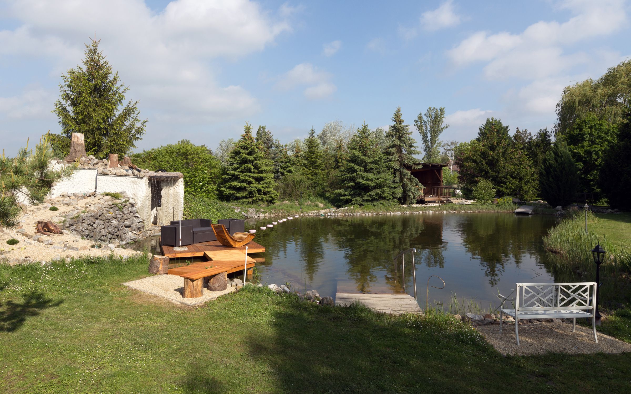 Ein idyllischer Gartenteich mit Sitzgelegenheiten und umgebender Vegetation.