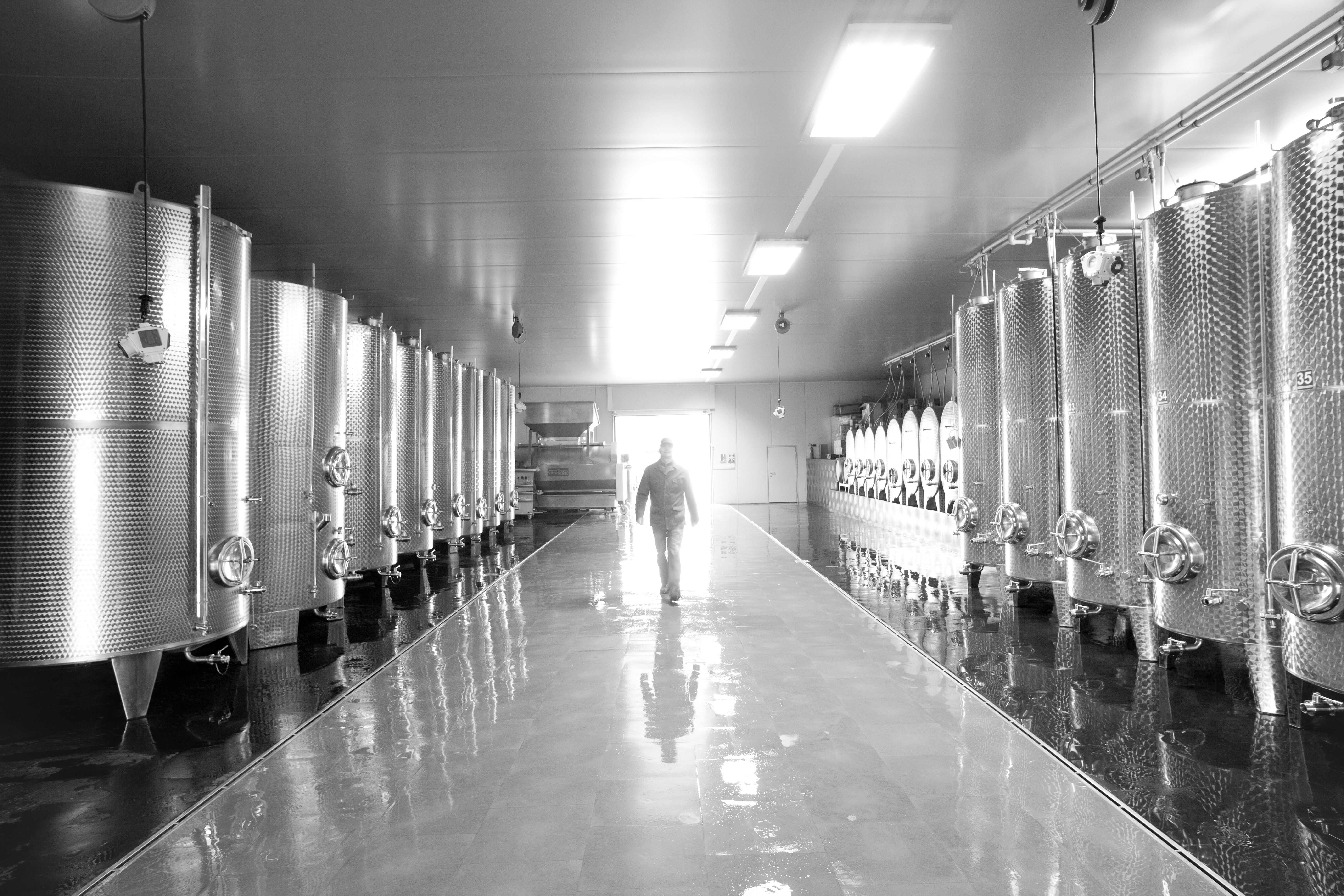 A man walks through a room with large stainless steel tanks.