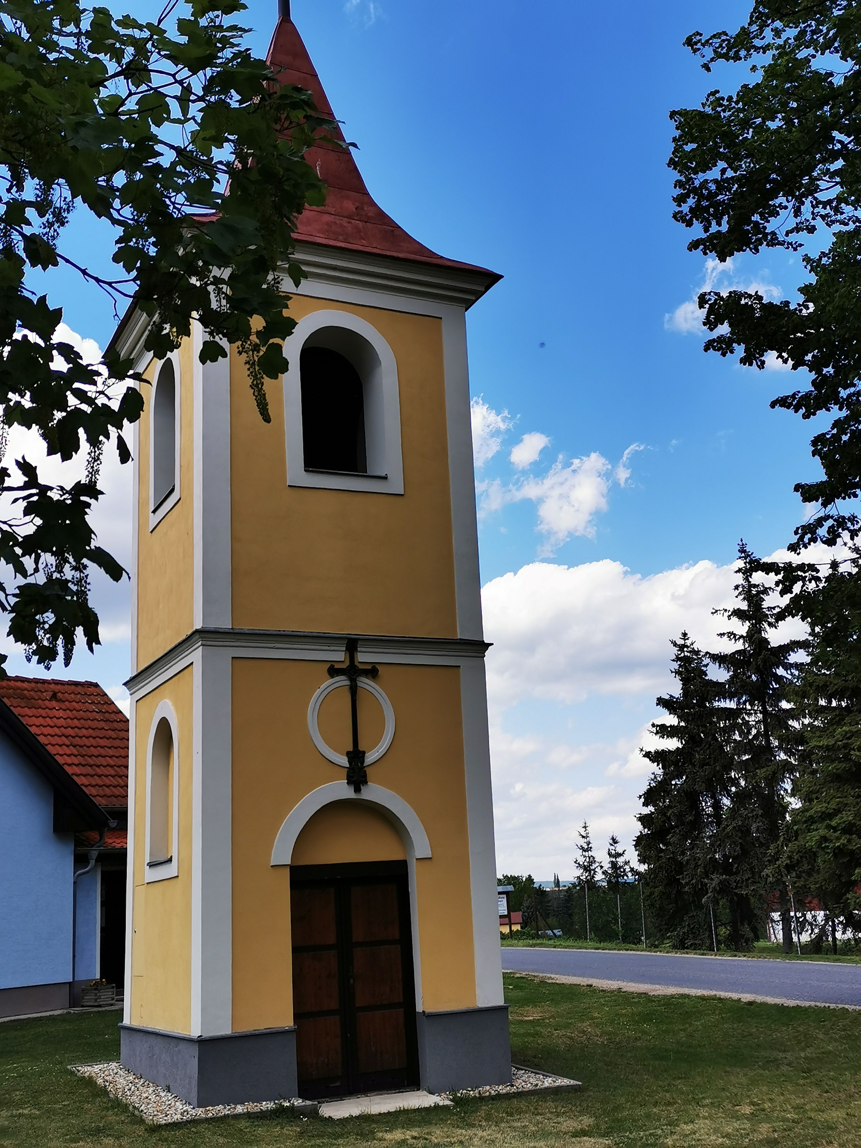 Zvonice v Ragelsdorfu na pozadí modré oblohy a stromů.