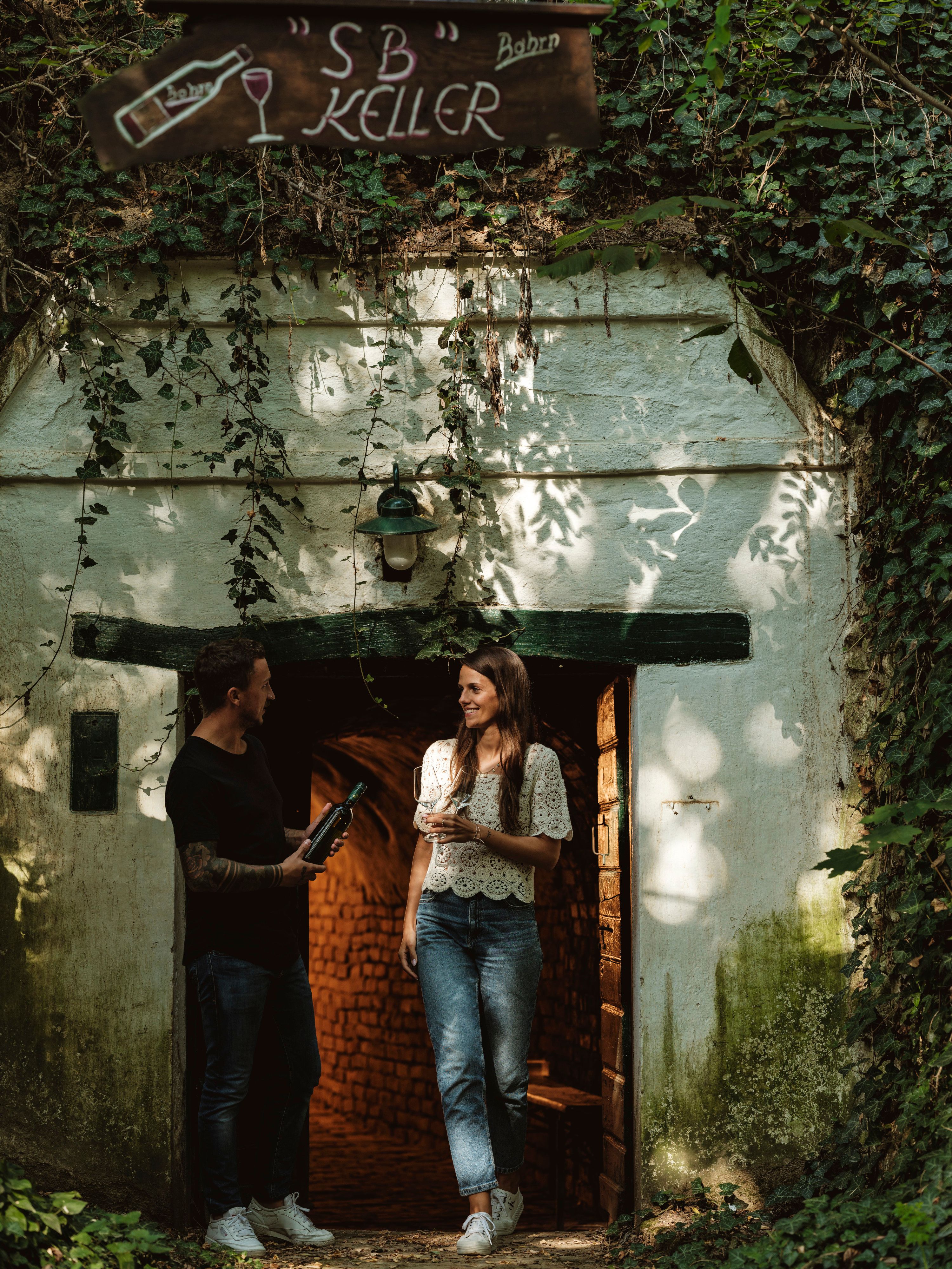A man and a woman are standing in front of a wine cellar labeled 'SB Keller'.