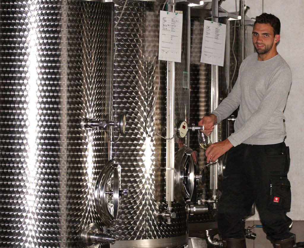 A man draws wine from a stainless steel tank in a wine cellar.