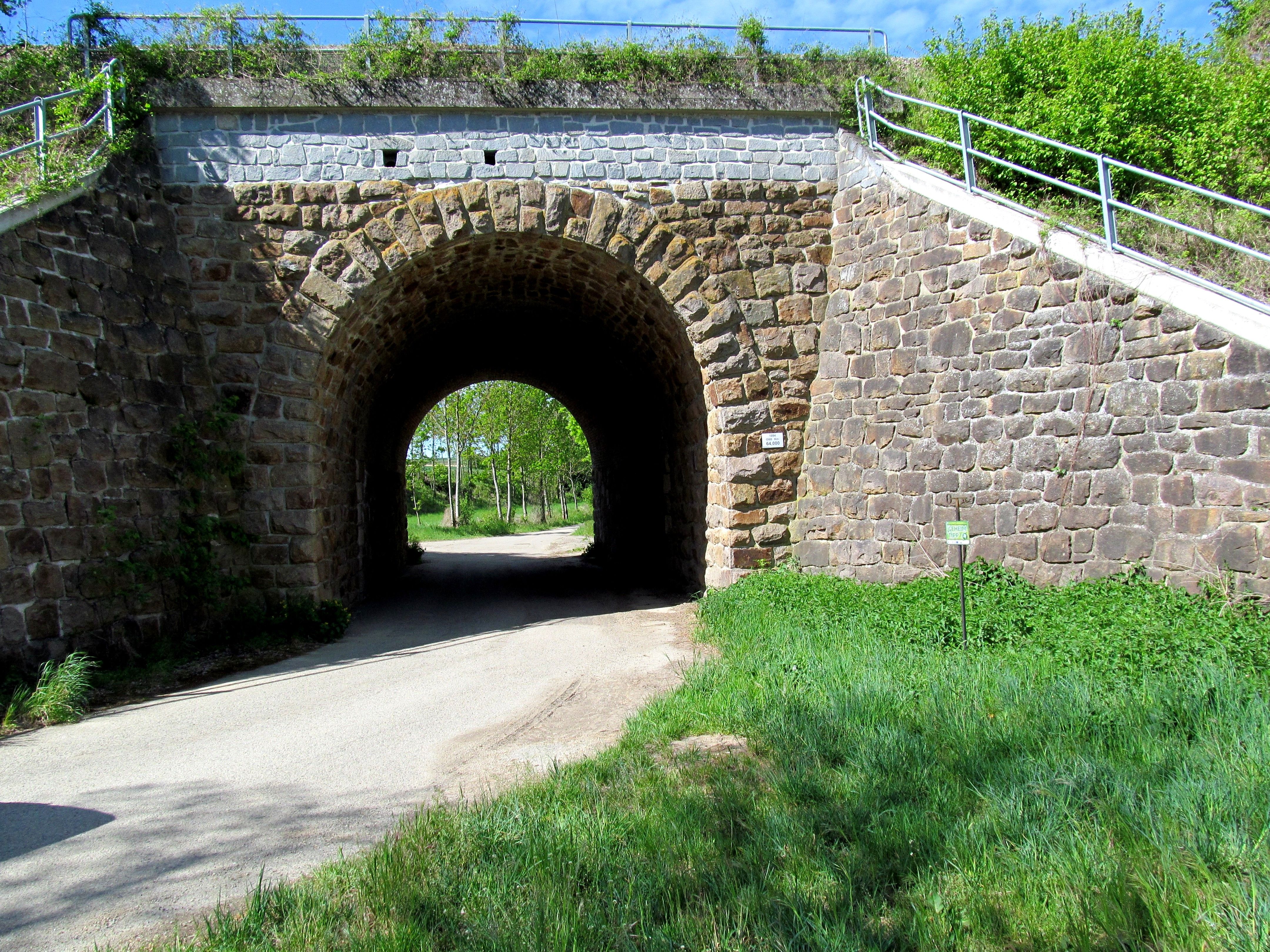 Steinviadukt mit Durchgang und grünem Umfeld.