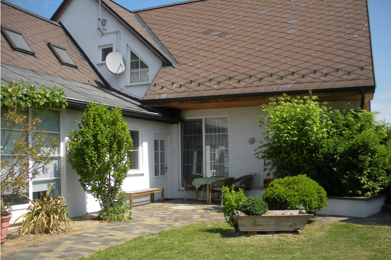 Ein gepflegter Innenhof mit Gartenmöbeln, Pflanzen und einem großen Dach mit Dachfenstern.