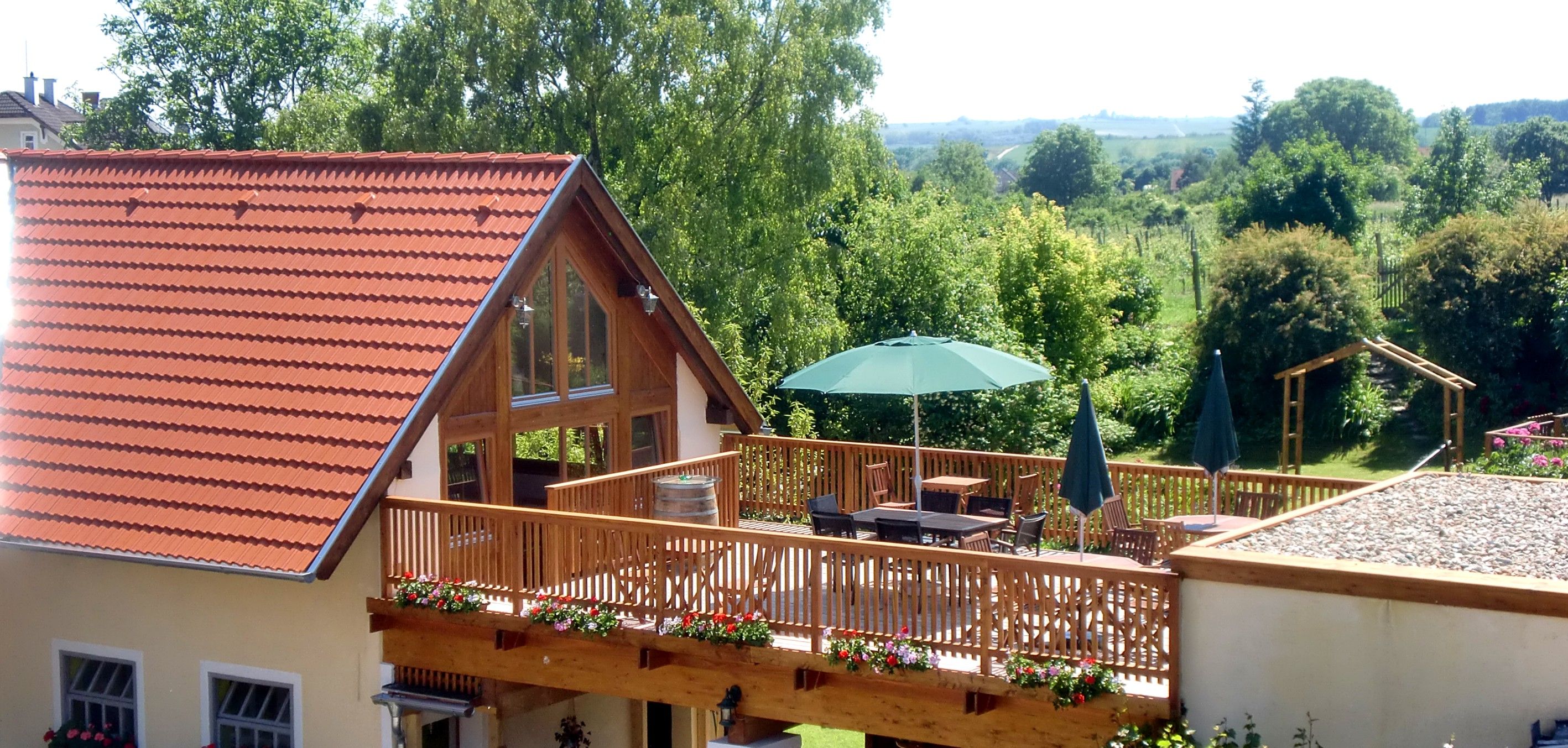 Terrace with wooden fence, parasol and garden furniture, surrounded by green countryside.