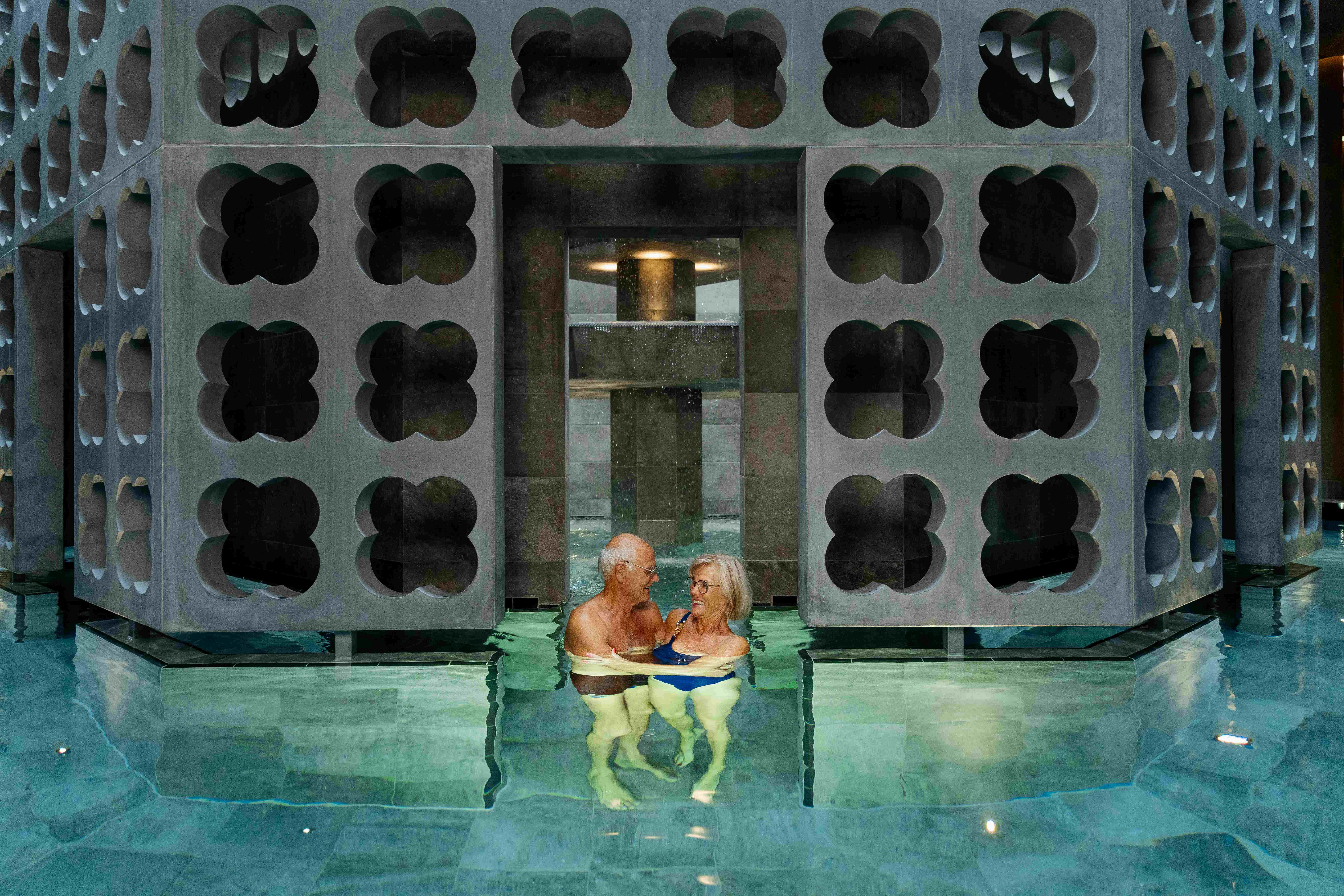 Ein älteres Paar genießt ein Thermalbad in einem modernen Spa mit geometrischen Strukturen.
