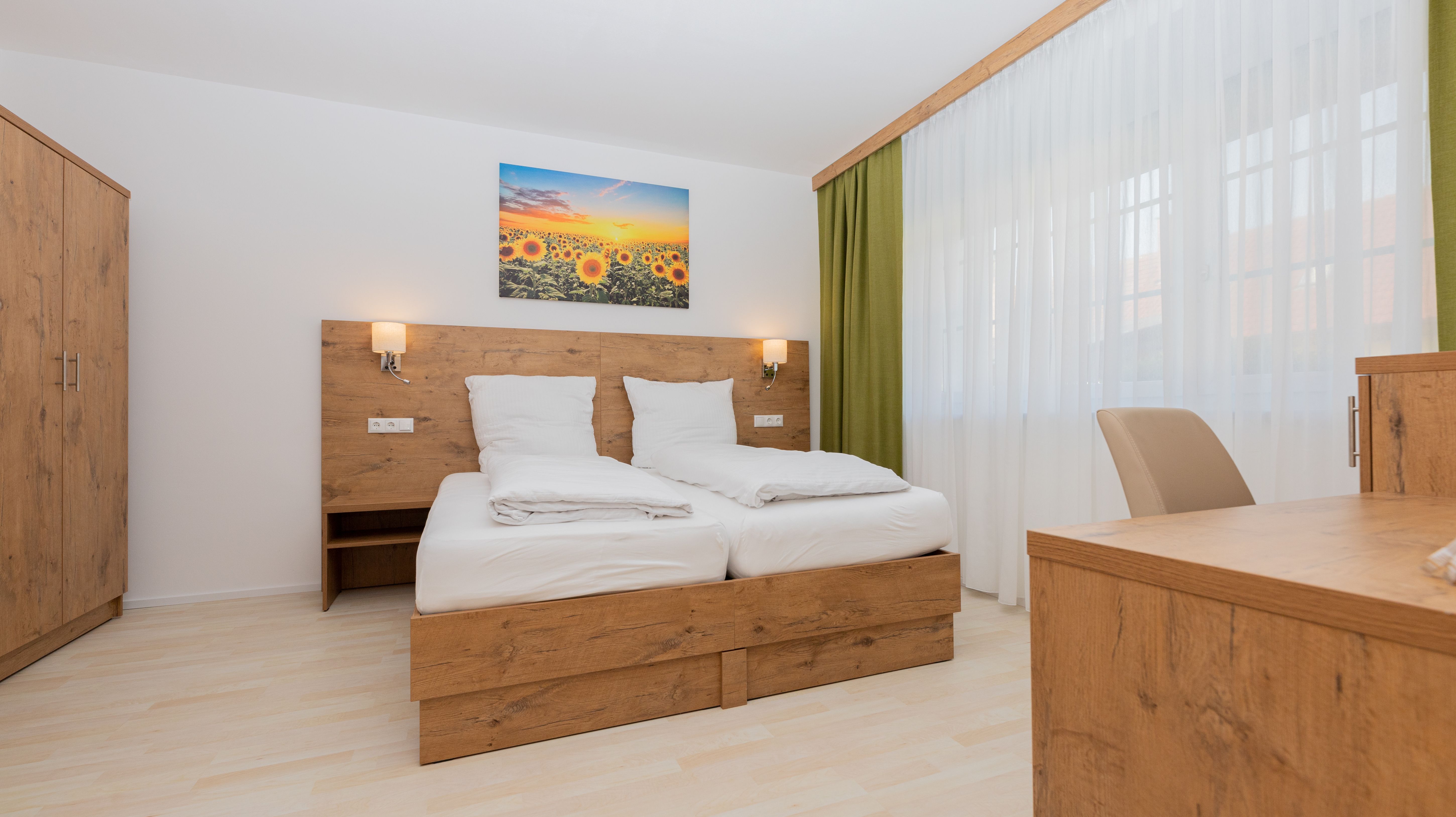 Modernes Schlafzimmer mit Holzmöbeln, Doppelbett, Schrank und Schreibtisch. Ein Bild mit Sonnenblumen hängt über dem Bett.