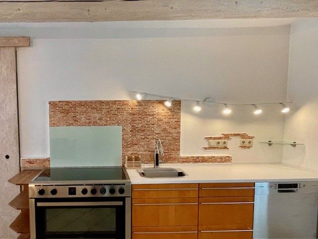 Moderne Küche mit Herd, Spüle und Geschirrspüler vor einer Mosaikfliesenwand.