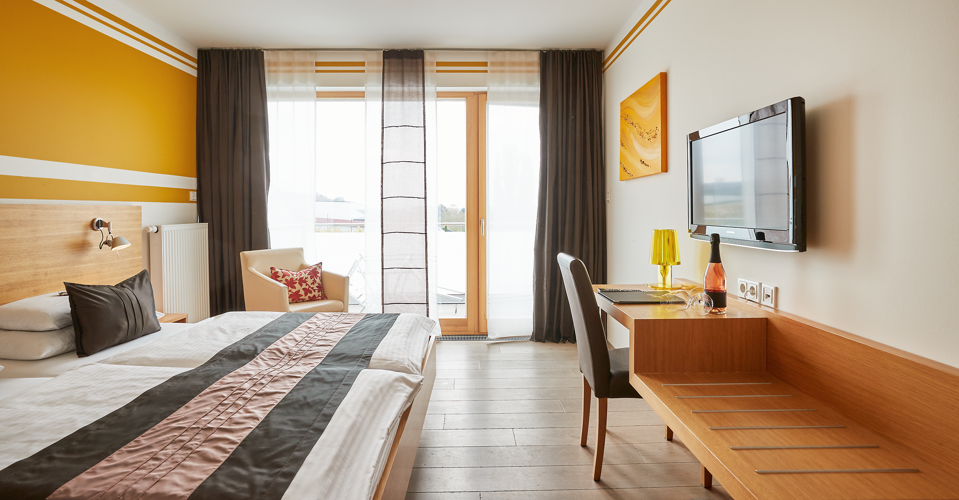 In einem einladenden Zimmer mit warmen Gelbtönen und modernem Design genießen Gäste die Ruhe und den Blick auf die Weinlandschaft. Die harmonische Atmosphäre lädt dazu ein, die Seele baumeln zu lassen und die Köstlichkeiten der Region zu entdecken.