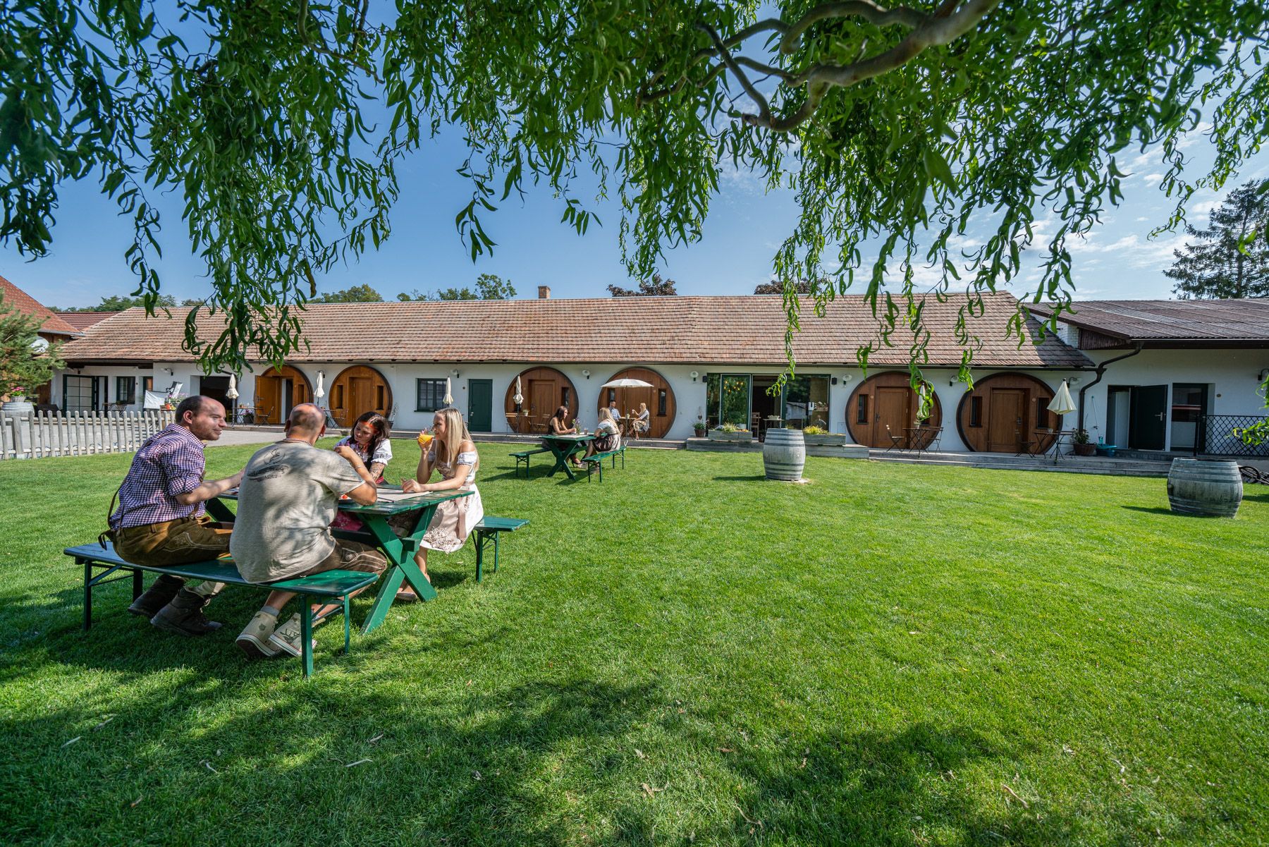 Menschen sitzen an einem Tisch auf einer Wiese vor einem Gebäude mit runden Türen.