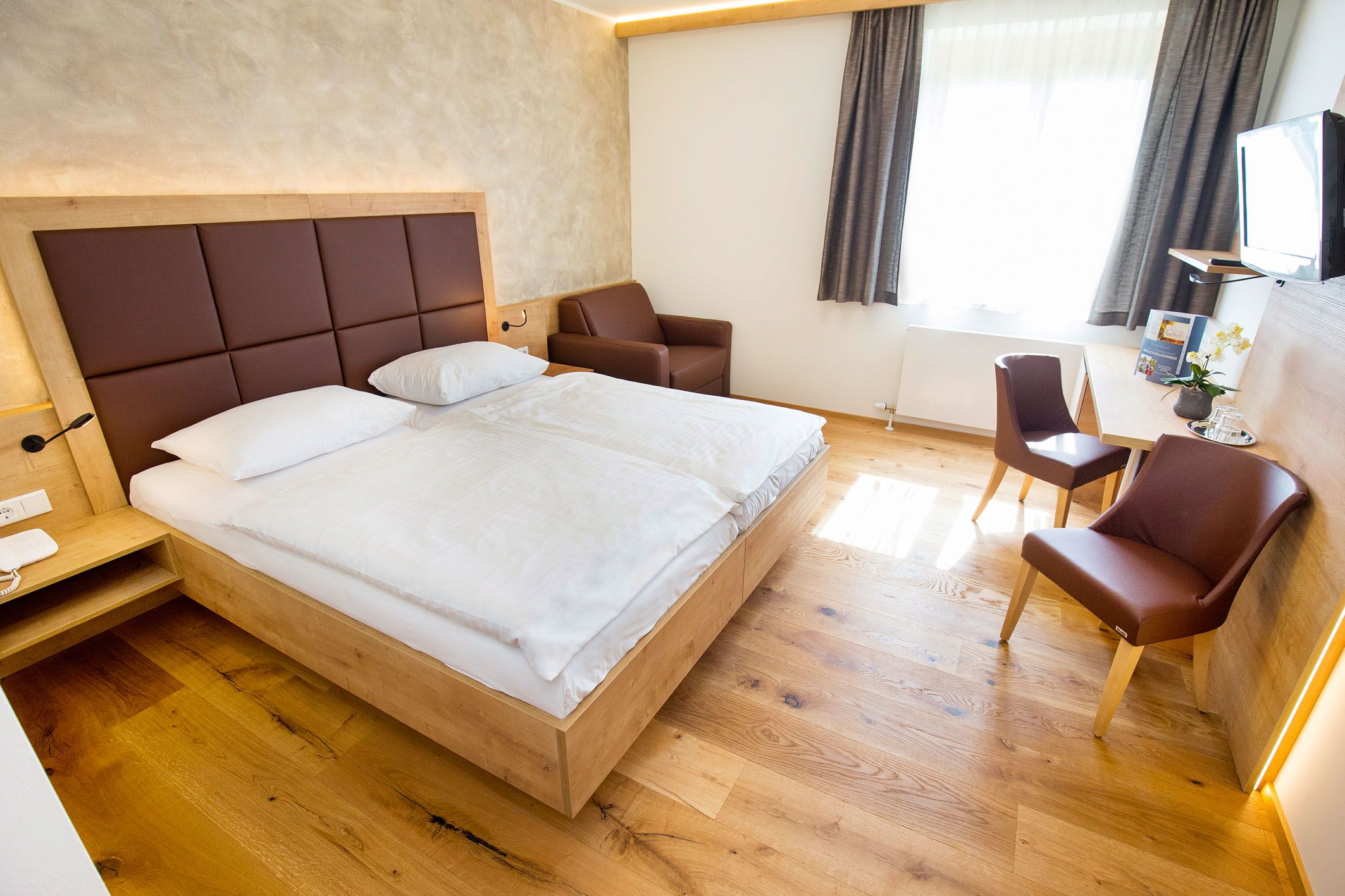 Modern eingerichtetes Hotelzimmer mit Doppelbett, Schreibtisch, Stühlen und einem Sessel.