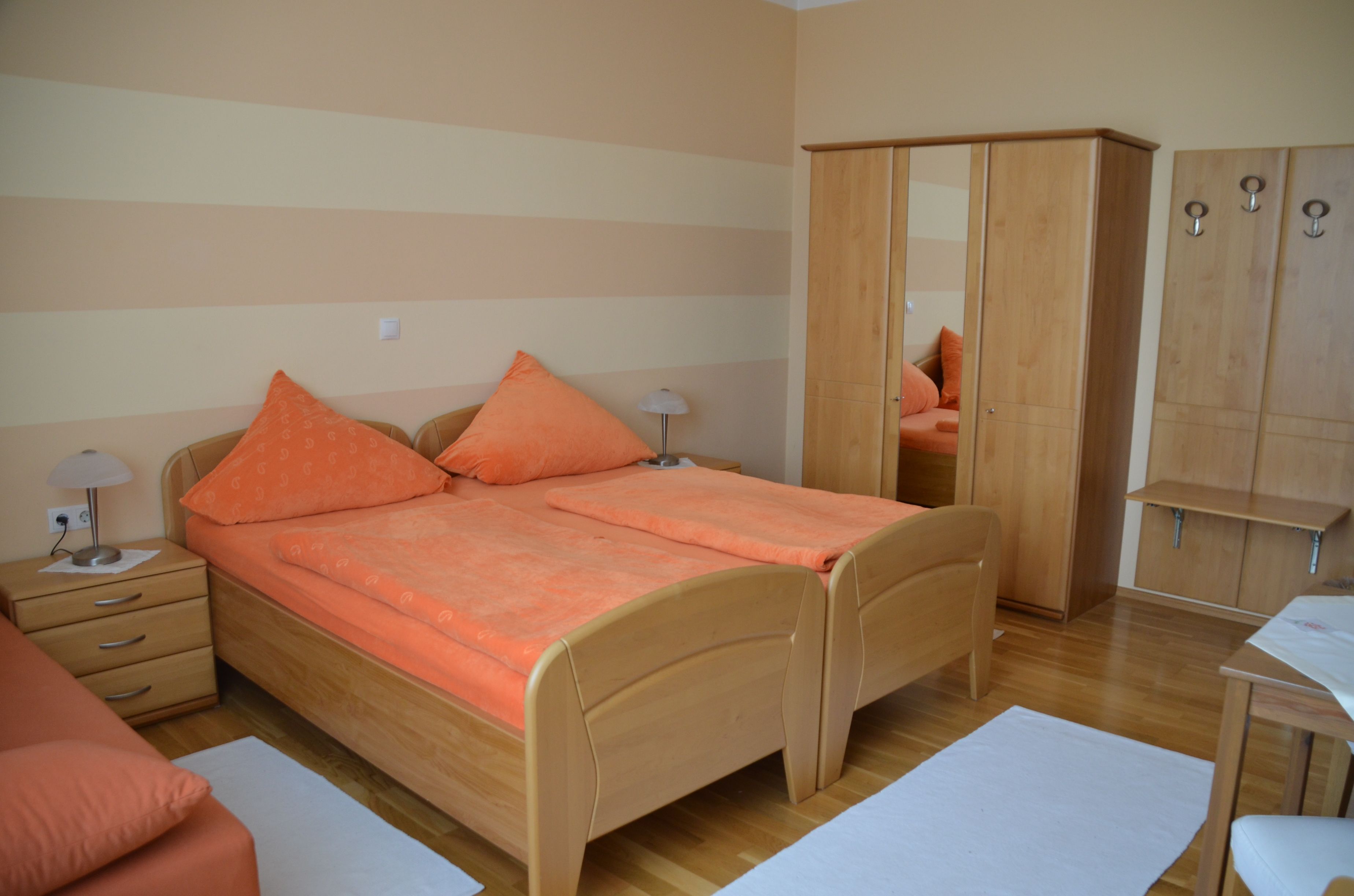 Ein gemütliches Schlafzimmer mit zwei Einzelbetten, orangefarbener Bettwäsche, einem Kleiderschrank und Nachttischen.