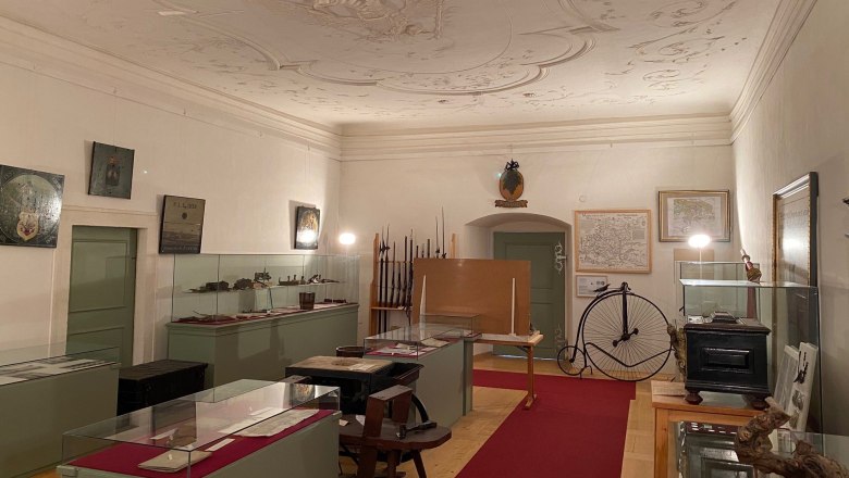 Innenansicht eines Museumsraums mit Vitrinen, alten Karten und einem Hochrad.