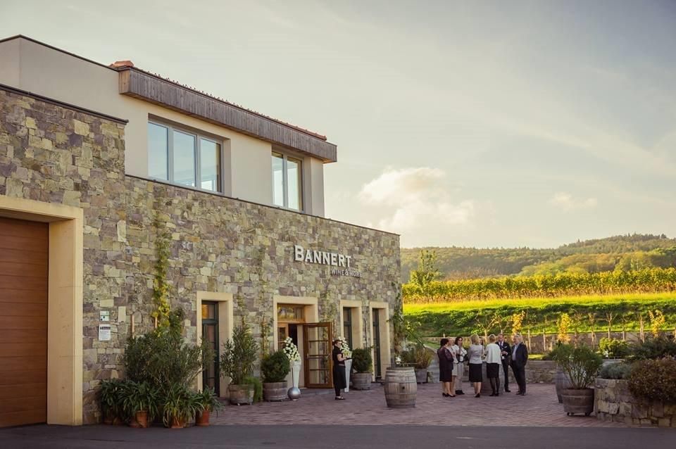 Weingut Bannert mit Menschen vor dem Gebäude und Weinbergen im Hintergrund.