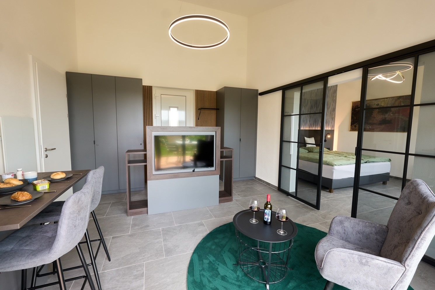 Modernes Apartment mit Esstisch, Fernseher, grauen Schränken und Glas-Schiebetüren zum Schlafzimmer.