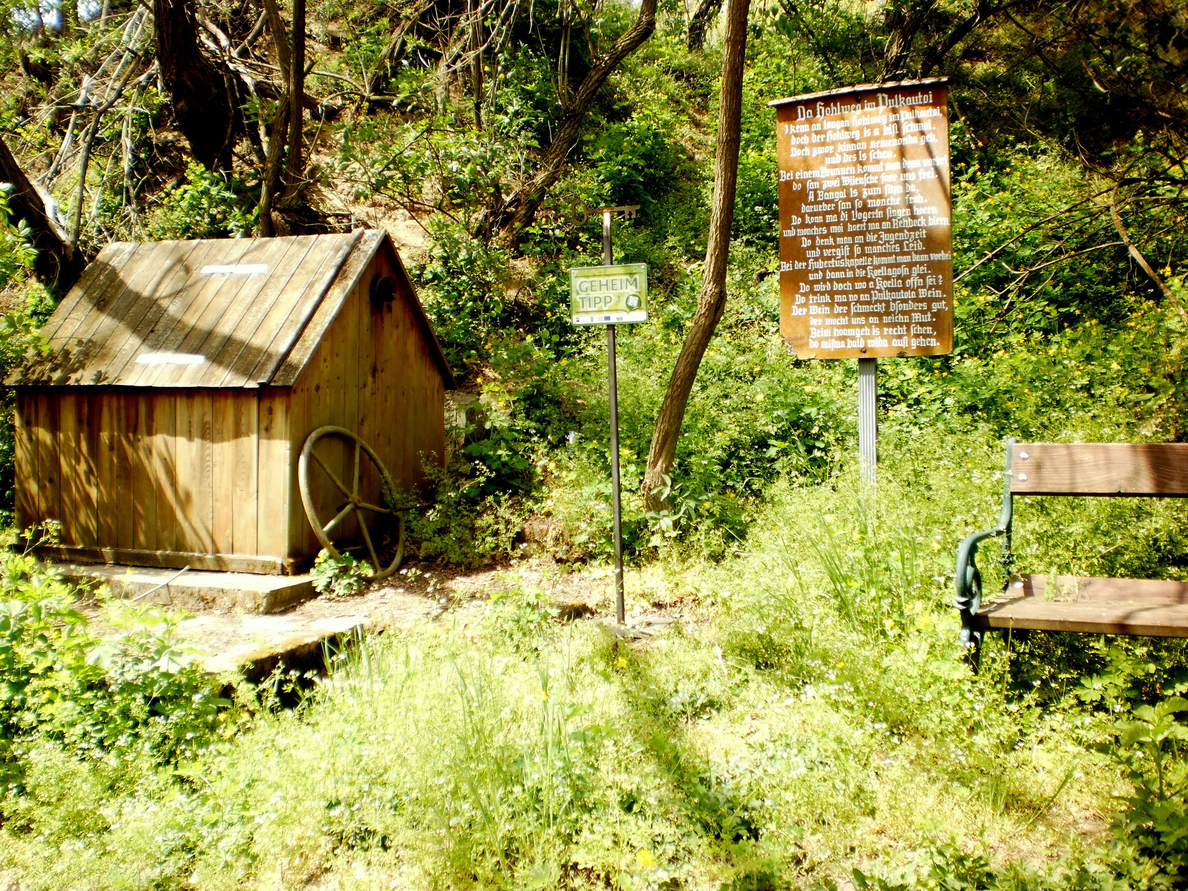 Holzhütte und Bank im Grünen mit Infotafel.