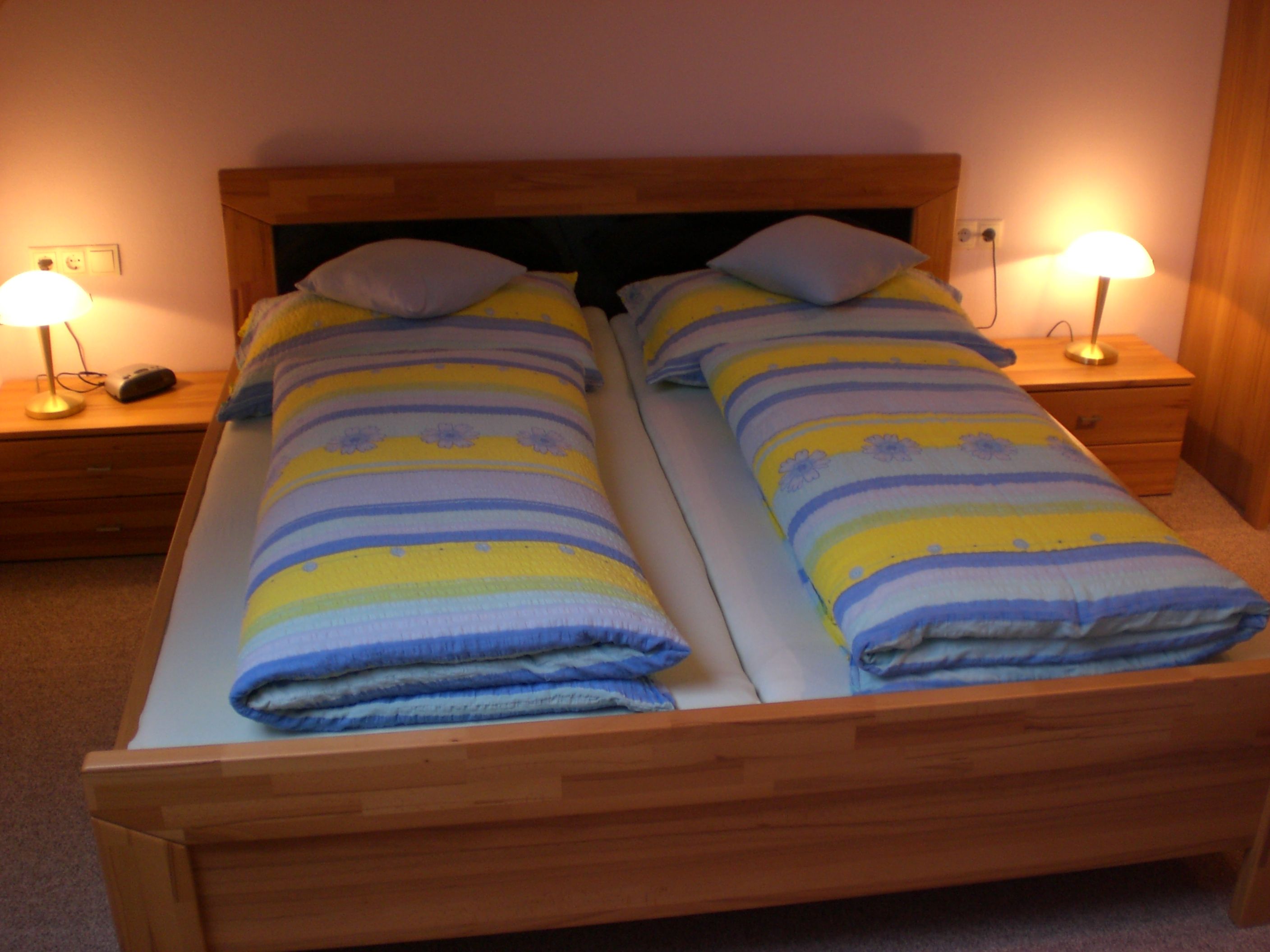 Ein gemütliches Gästezimmer mit einem Doppelbett, bunten Bettdecken und zwei Nachttischen mit Lampen.