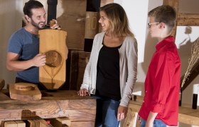 Drei Personen stehen um einen Holztisch, eine Person hält ein Holzbrett mit Gravur.