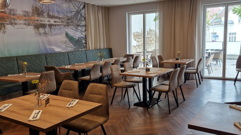 Innenansicht eines modernen Restaurants mit Holzboden, Tischen und Stühlen.