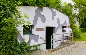 Eingang des Erdstallmuseums Alth&ouml;flein mit einem Mann, der die T&uuml;r zeigt.