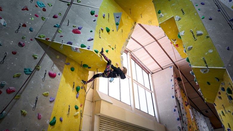 Person klettert an einer Indoor-Kletterwand mit bunten Griffen.