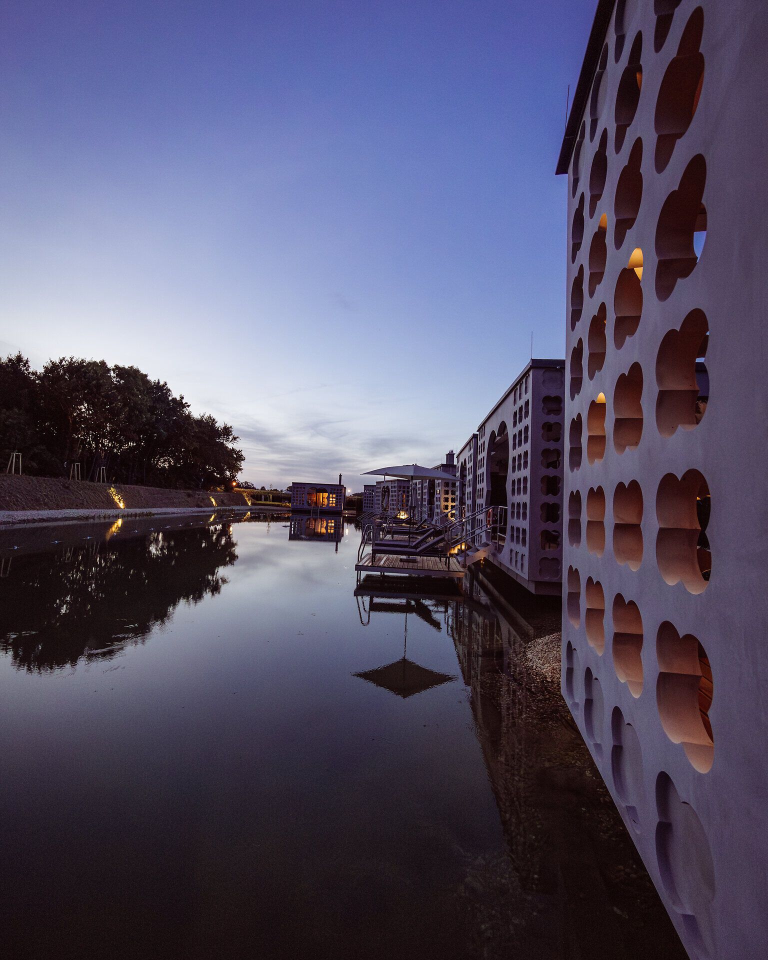 Die sanften Wellen des Wassers spiegeln die ruhige Abendstimmung wider, während die stilvollen Villen harmonisch am Ufer stehen. Hier, wo Entspannung und Natur aufeinandertreffen, lädt die Umgebung dazu ein, die Seele baumeln zu lassen und den Alltag hinter sich zu lassen.