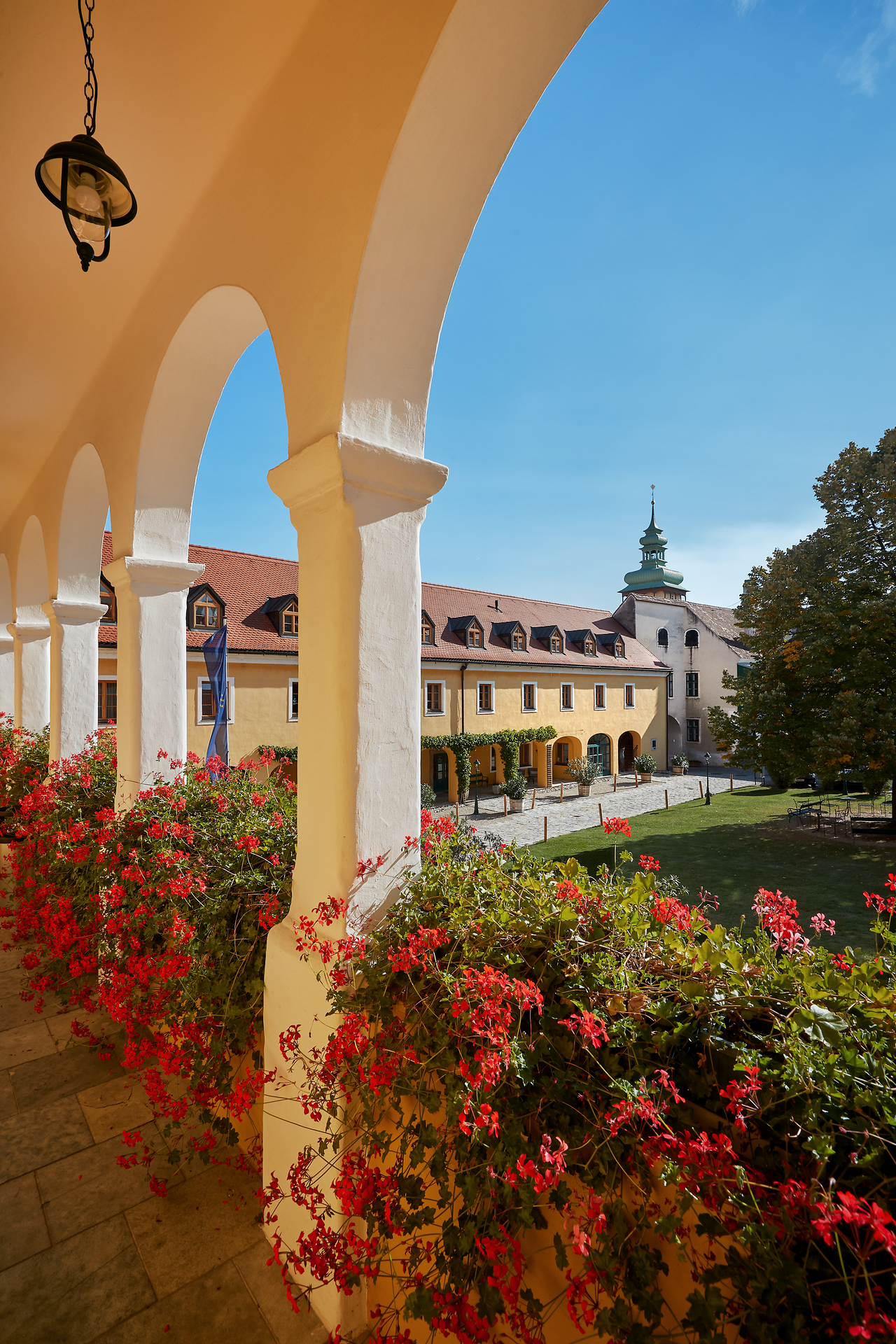 Die blühenden Geranien verleihen dem historischen Innenhof eine einladende Atmosphäre, während die sanften Farben der Gebäude im Sonnenlicht erstrahlen. Hier, umgeben von der malerischen Landschaft des Weinviertels, können Besucher die Ruhe und Schönheit der Natur genießen.
