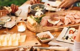 Ein gedeckter Tisch mit Brot, Käse, Aufschnitt und Weingläsern.
