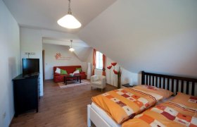 Gemütliches Gästezimmer mit Doppelbett, Sofa, Fernseher und dekorativen Elementen.