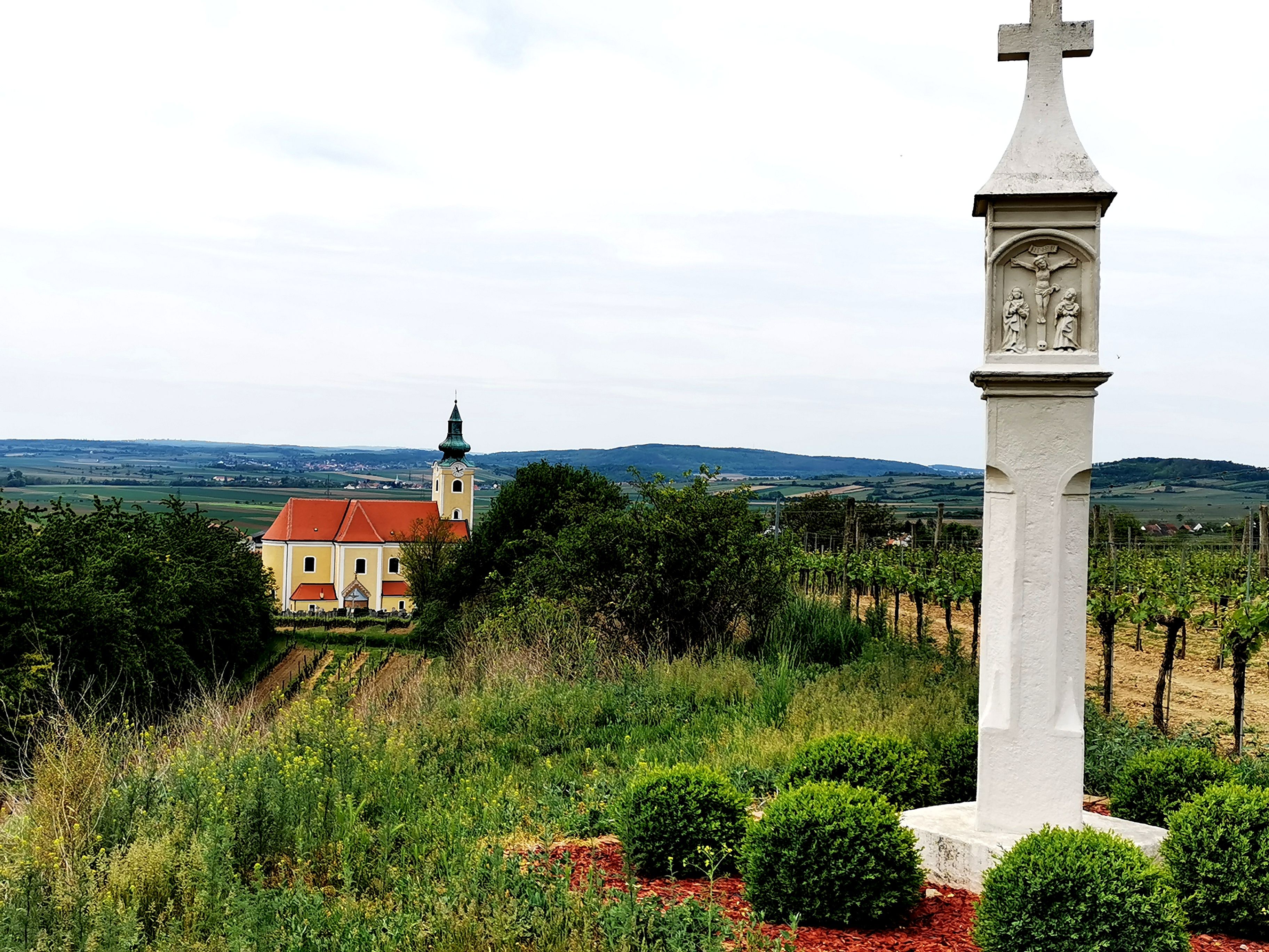 Landschaft mit Kirche und Steinsäule im Weinviertel, Österreich.