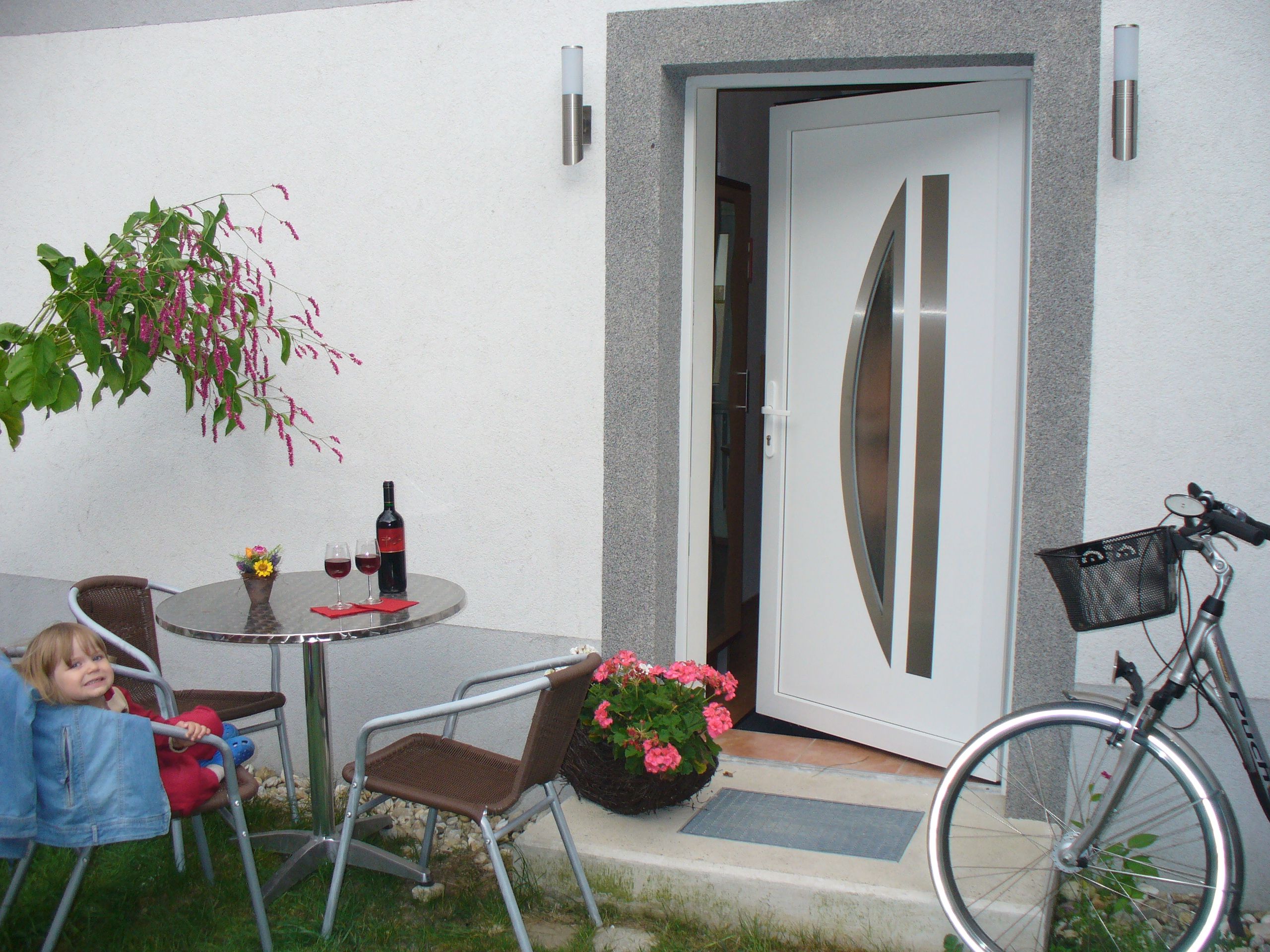 Ein offener Hauseingang mit Tisch, Stühlen, Weinflasche und Fahrrad.