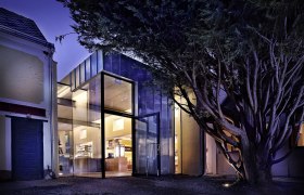 Moderne Glasfassade eines Gebäudes bei Nacht, umgeben von Bäumen.