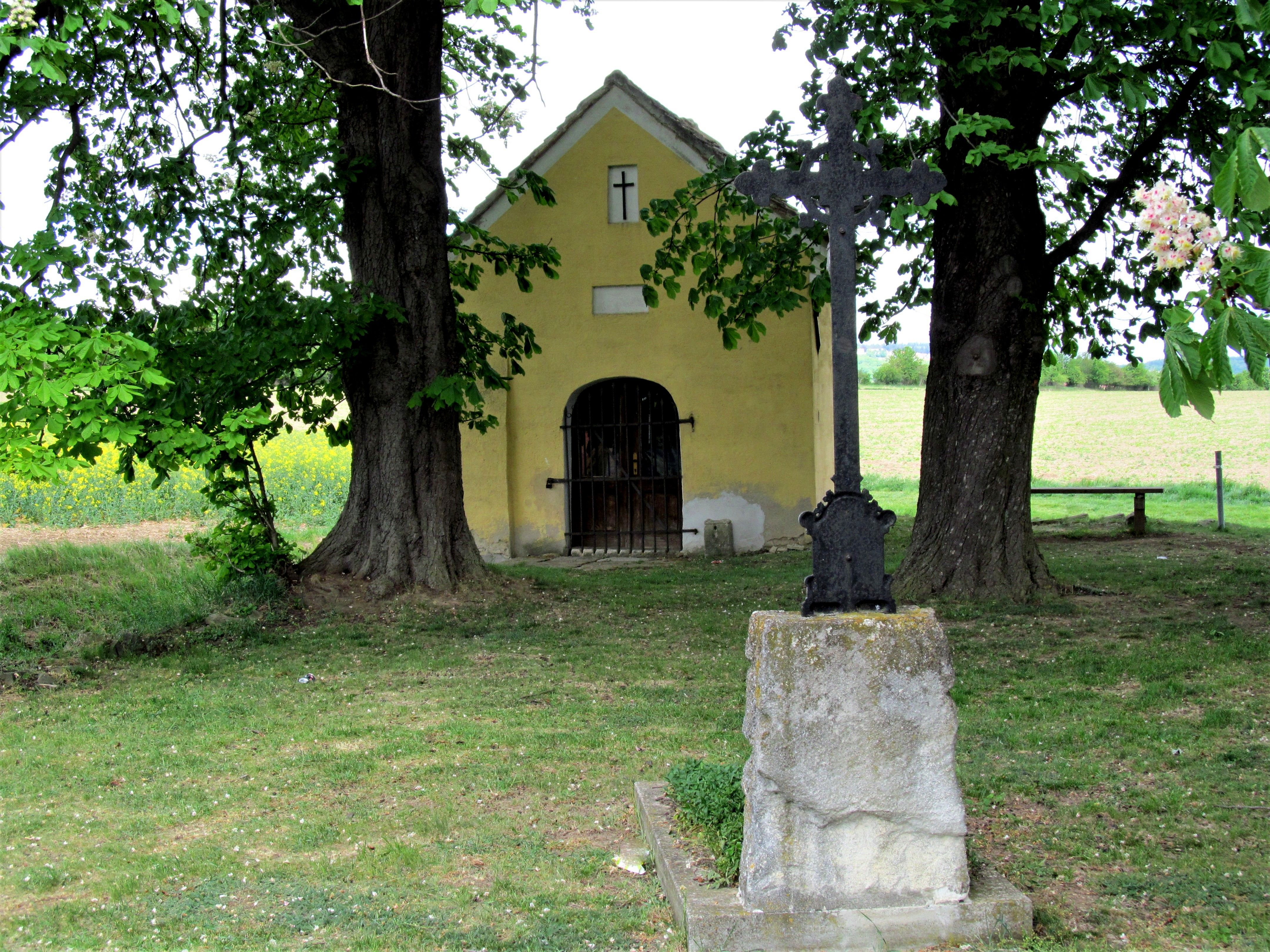 Gelbe Kapelle mit Kreuz und Bäumen im Vordergrund.