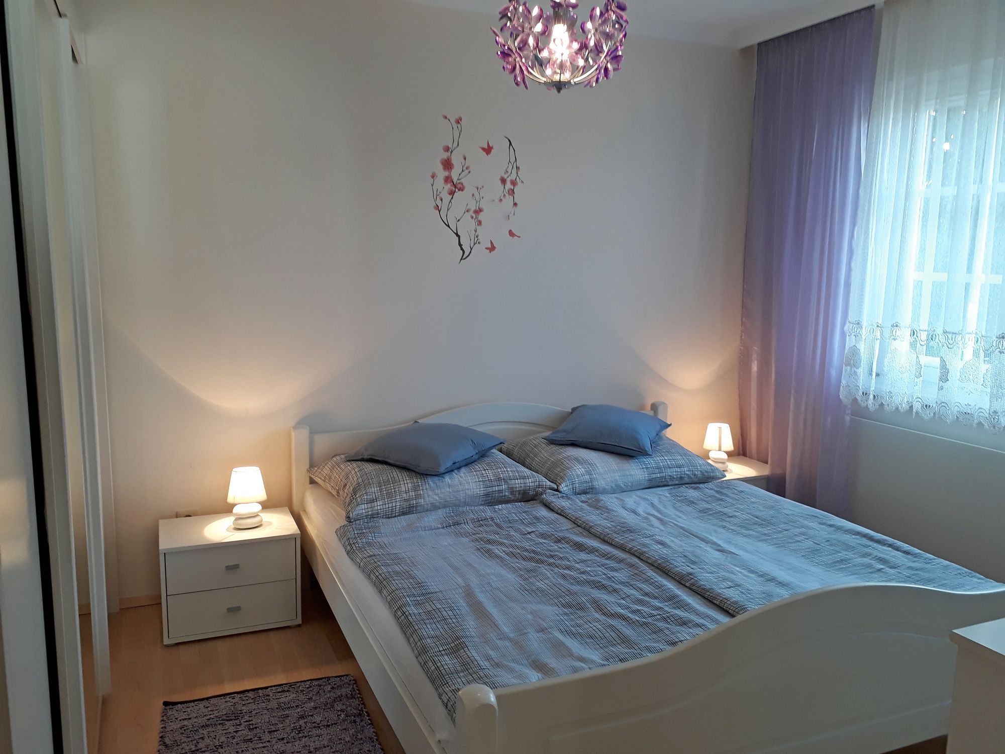 Ein gemütliches Schlafzimmer mit Doppelbett, zwei Nachttischen mit Lampen und lila Vorhängen.