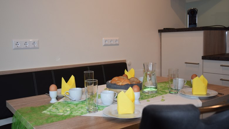 Fr&uuml;hst&uuml;ckstisch mit Br&ouml;tchen, Eiern, Tassen und gelben Servietten.