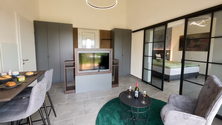 Modernes Apartment mit Esstisch, Fernseher, grauen Schränken und Glas-Schiebetüren zum Schlafzimmer.