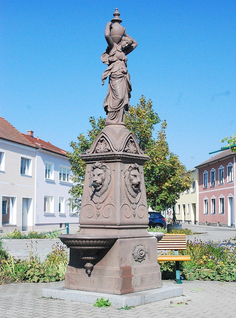 Brunnen mit Statue und Löwenköpfen auf einem Platz in Haugsdorf.