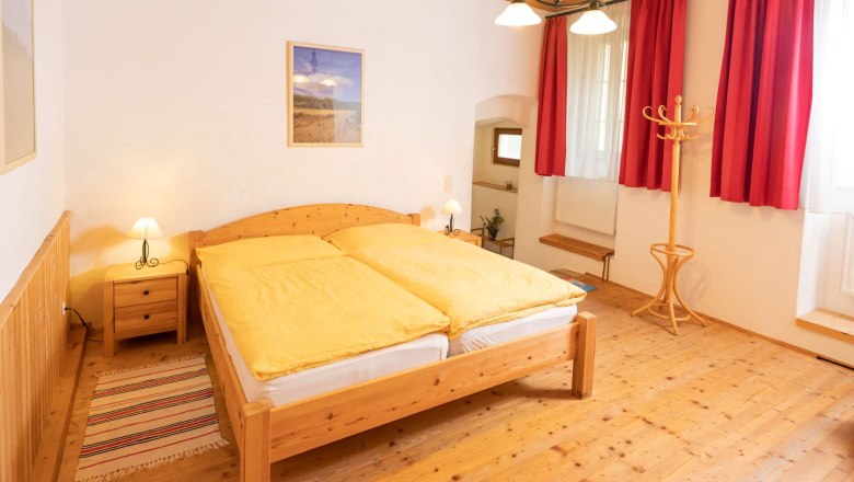 Gemütliches Schlafzimmer mit Holzmöbeln, gelber Bettwäsche und roten Vorhängen.