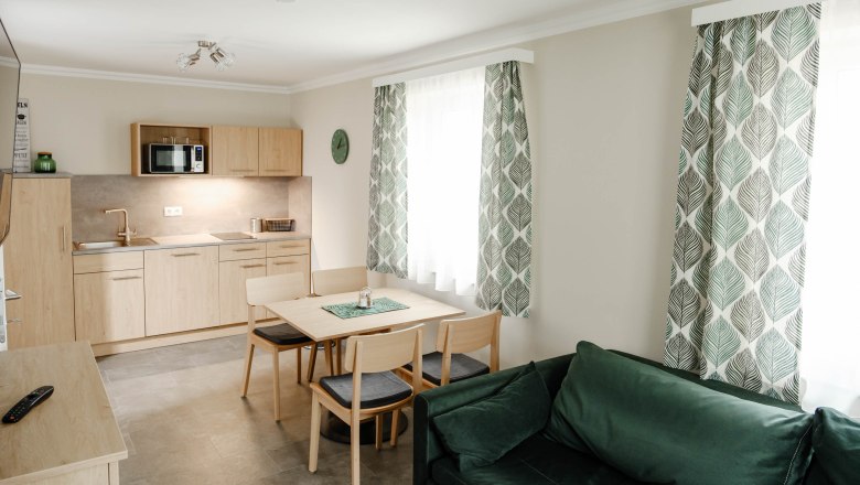 Moderne Küche mit Holzmöbeln, Esstisch, grünen Vorhängen und Sofa.