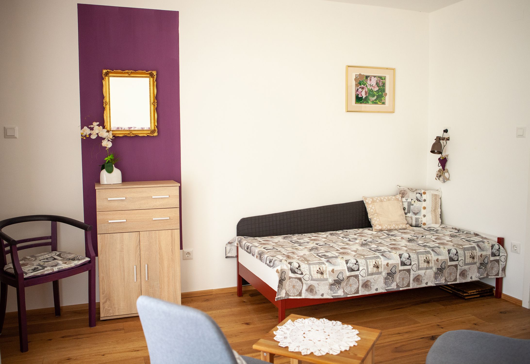 Ein Wohnzimmer mit einer Schlafcouch, einem kleinen Schrank, einem Stuhl und einem Tisch auf Holzboden.