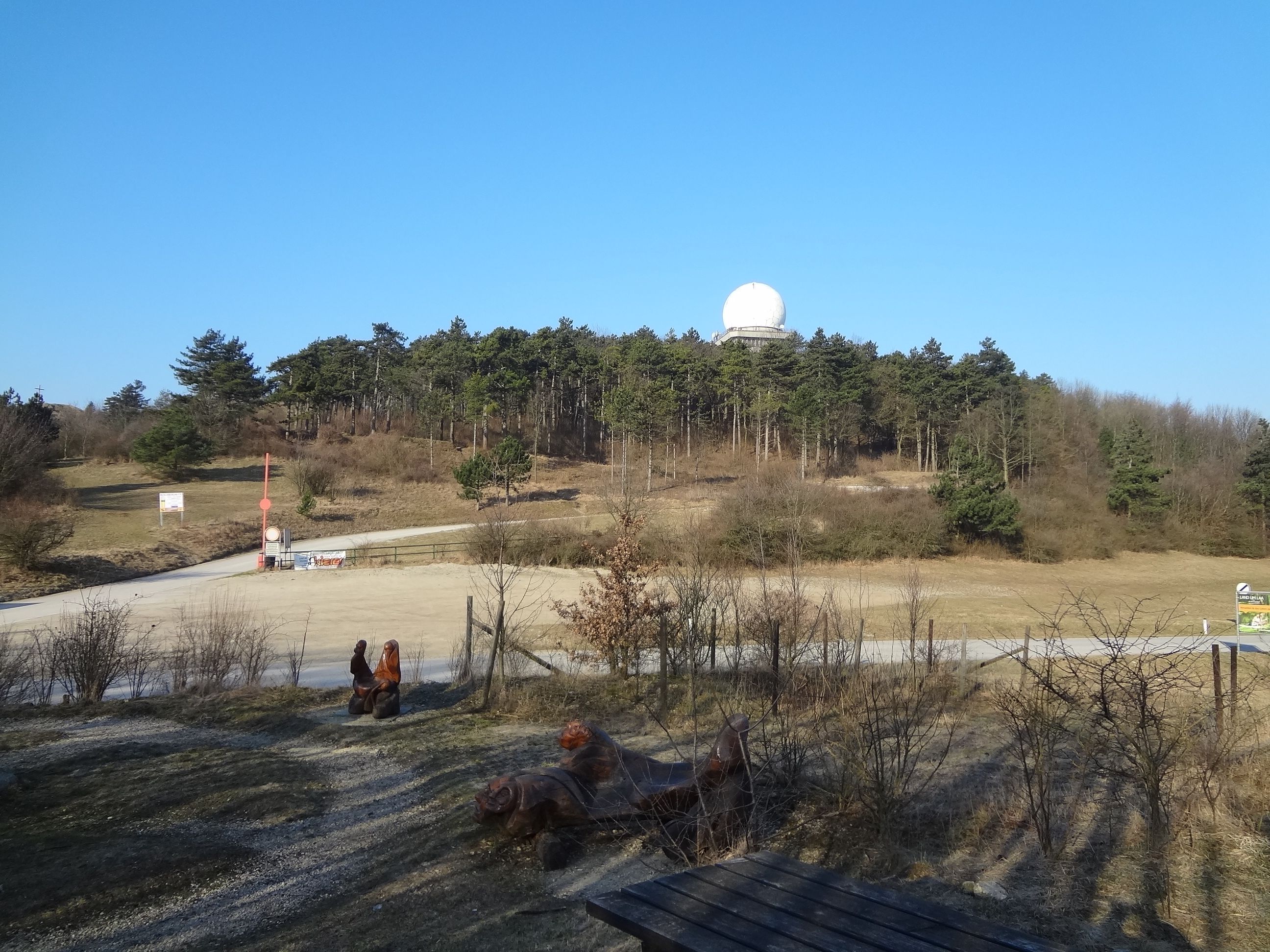 Landschaft mit Hügel, Wald und Radarkuppel unter blauem Himmel.